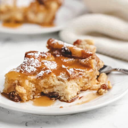 A piece of Irish bread pudding on a plate with a bite on a fork.