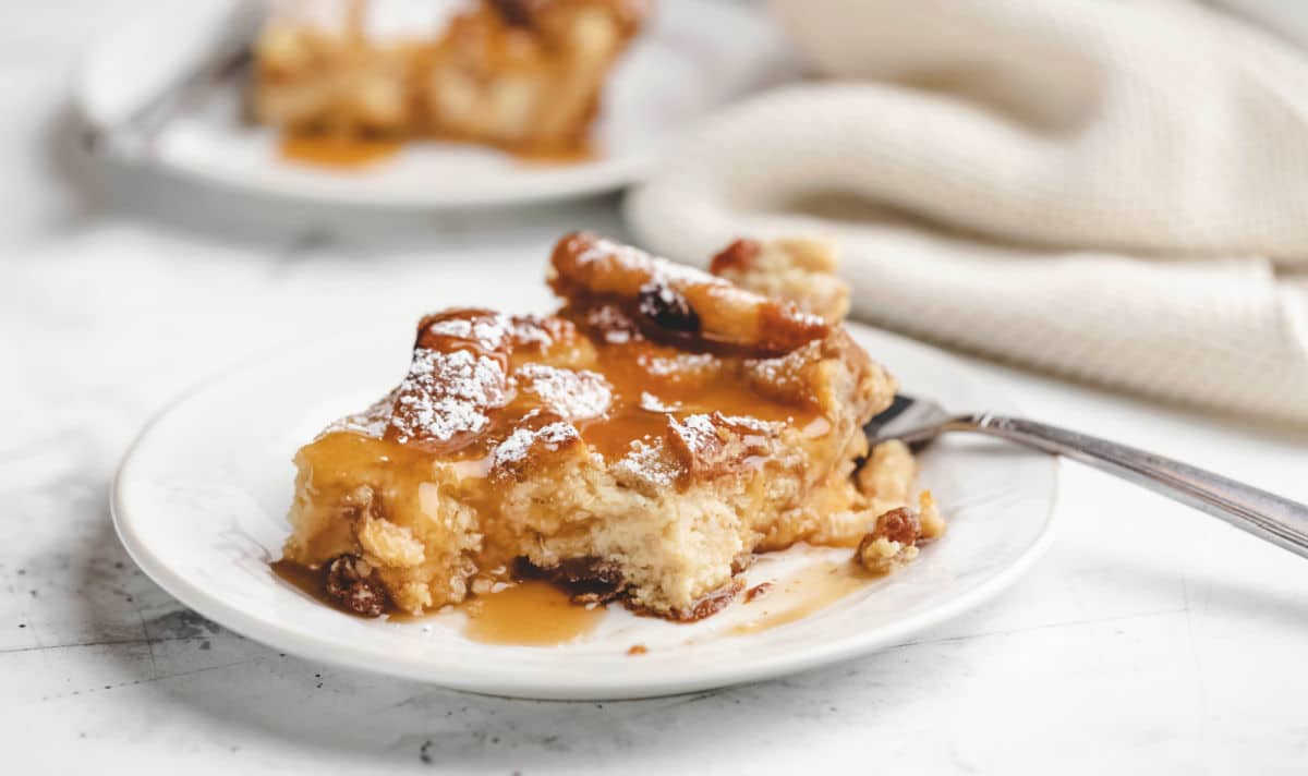 A piece of Irish bread pudding on a plate with a bite on a fork. 