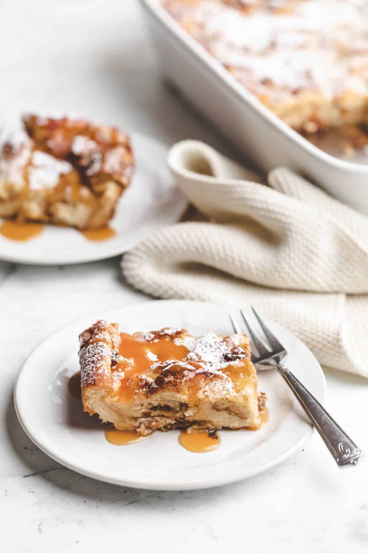 A piece of Irish bread pudding topped with caramel sauce and powdered sugar.