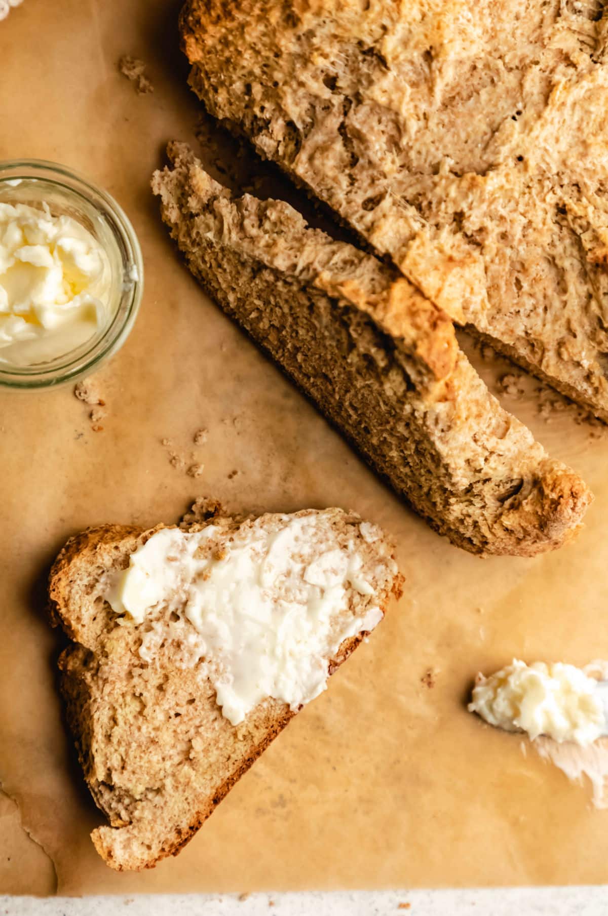 A half buttered slice of Irish brown soda bread next to a dish of butter. 