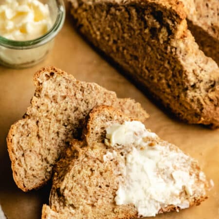 Two slices of Irish brown soda bread with one slice partially buttered.