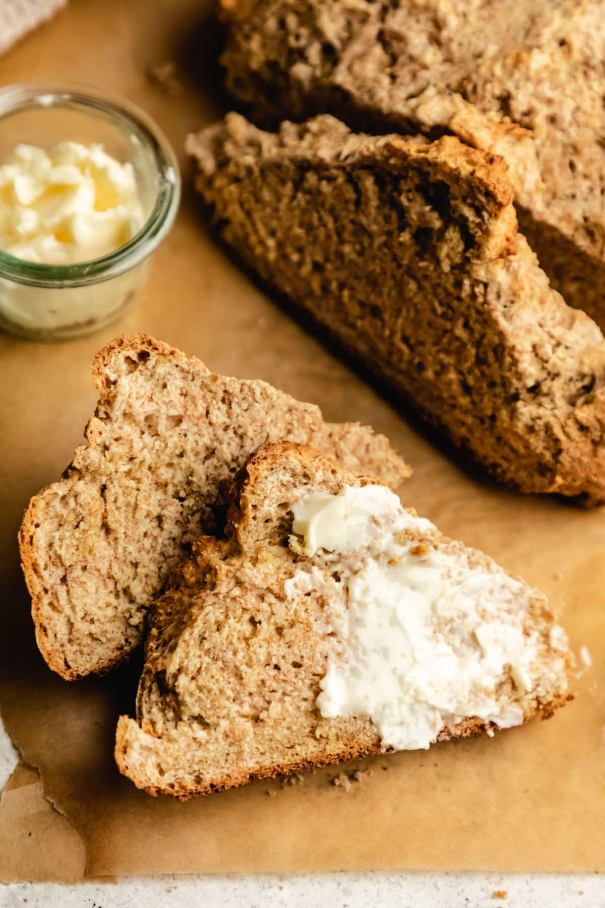 Two slices of Irish brown soda bread with one slice partially buttered.