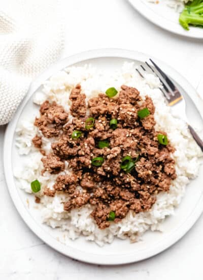 Korean ground beef over rice on a white plate with a silver fork.