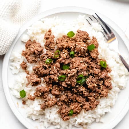 Korean ground beef over rice on a white plate with a silver fork.