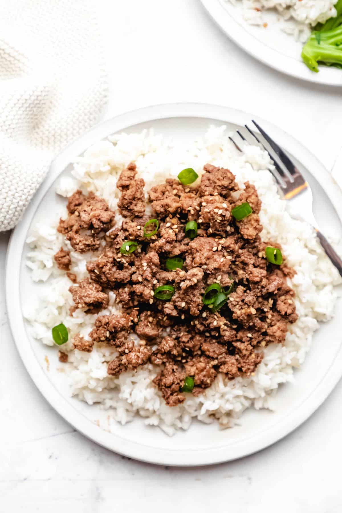 Korean ground beef over rice on a white plate with a silver fork.