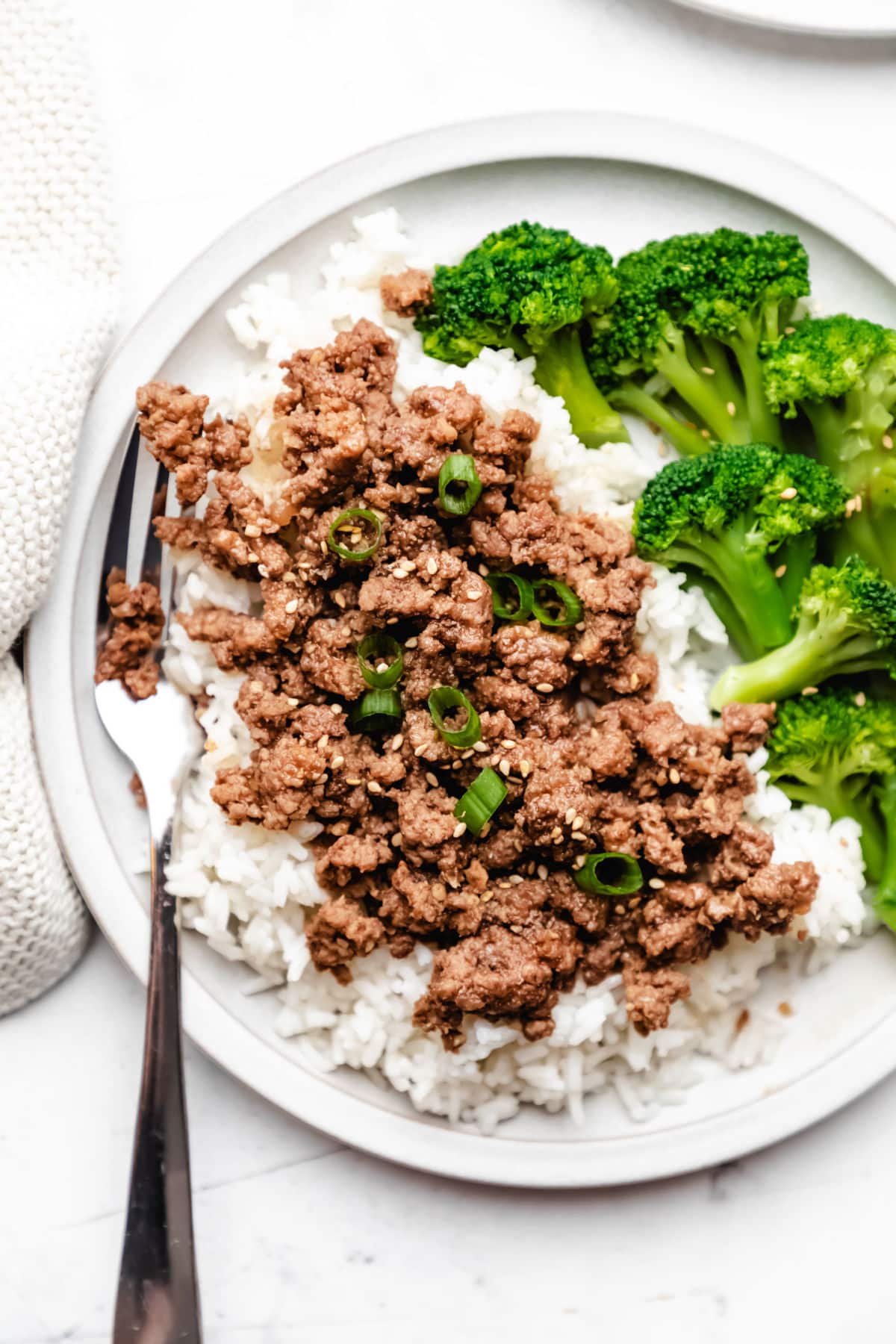 Korean ground beef topped with green onions next to rice and steamed broccoli. 