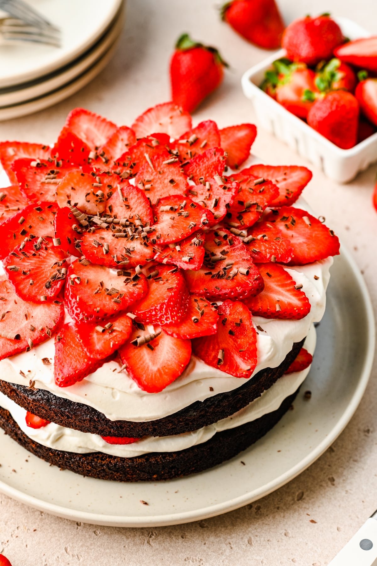 Chocolate strawberry cake next to a stack of plates. 