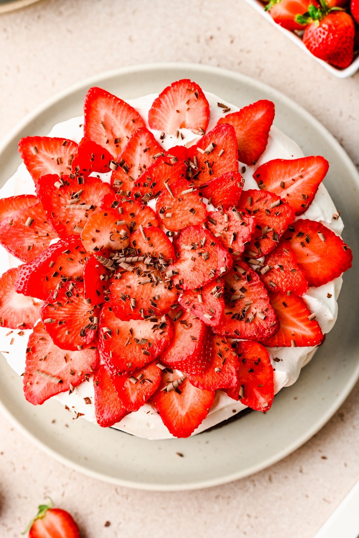 Chocolate shavings on chocolate strawberry cake next to a carton of strawberries. 