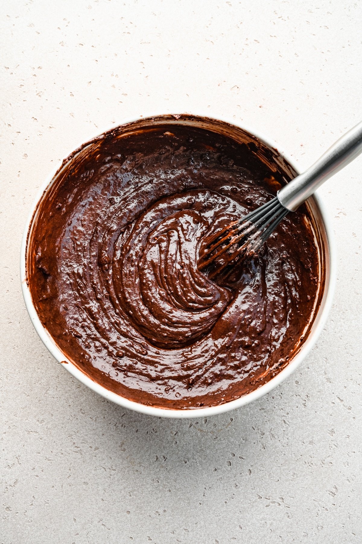 Chocolate cake batter in a mixing bowl with a whisk in it. 