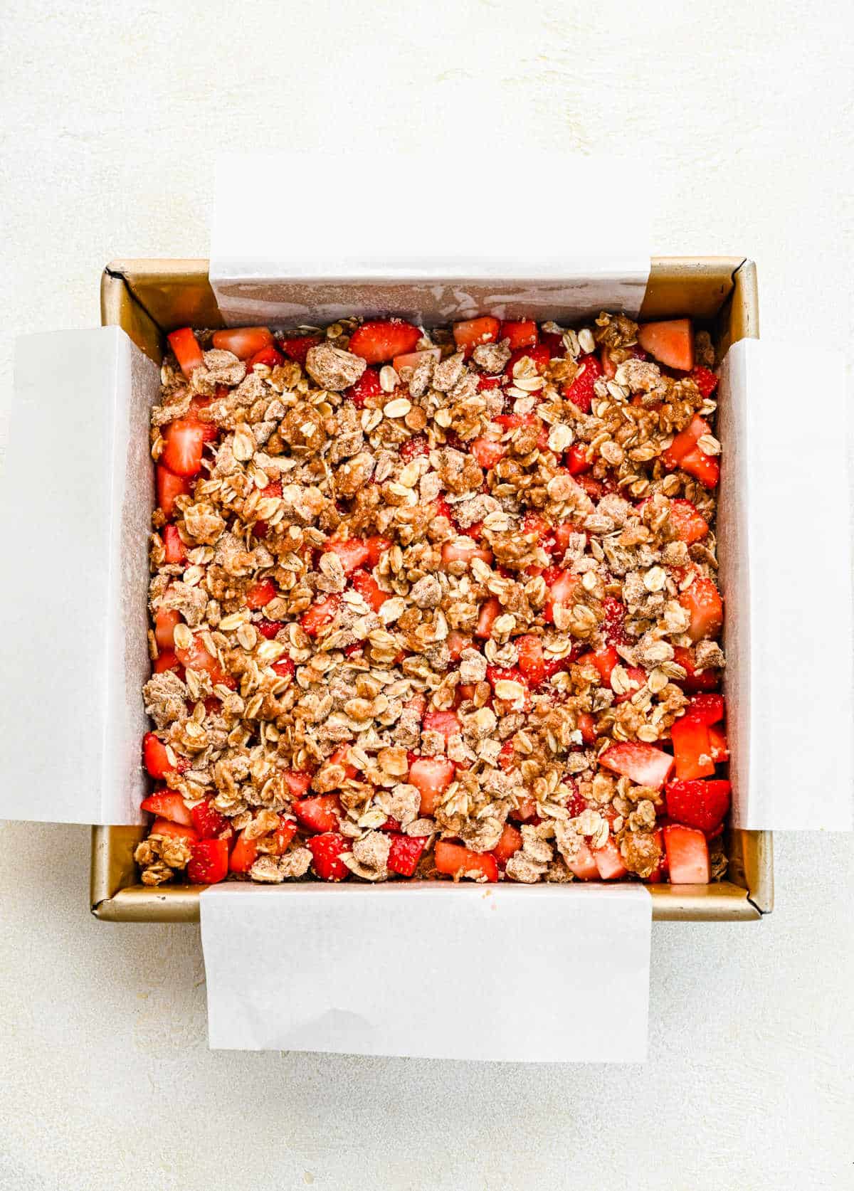 Oatmeal crumble on top of strawberries in a baking pan.