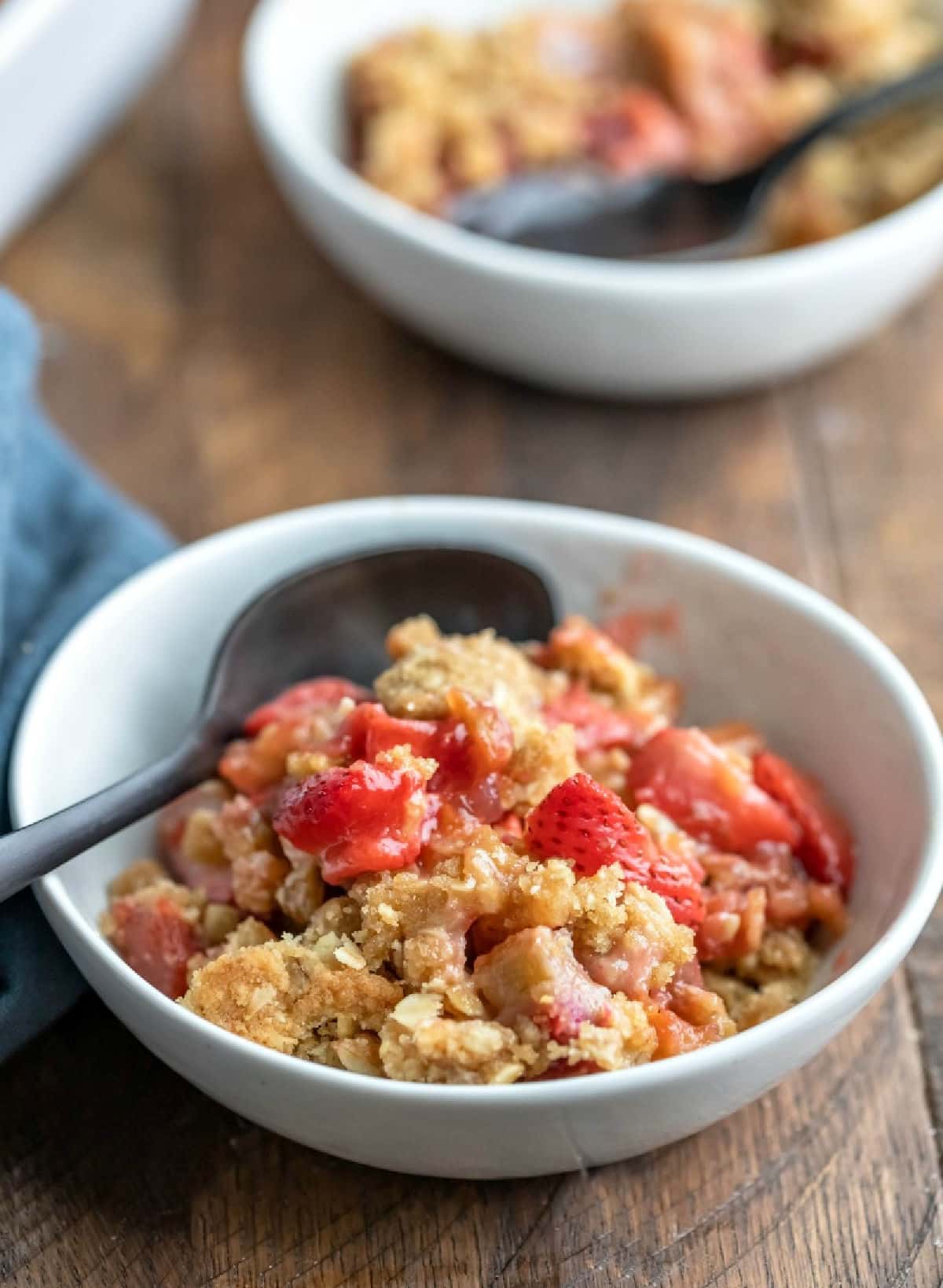 A dish of strawberry rhubarb crisp with a black spoon in it. 