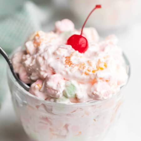 A glass dish of ambrosia salad topped with a maraschino cherry.