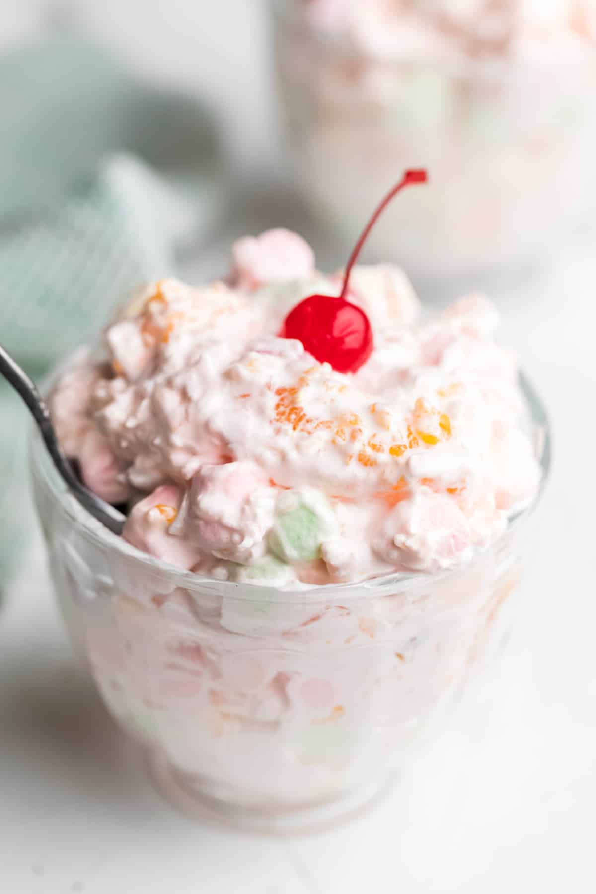 A glass dish of ambrosia salad topped with a maraschino cherry. 