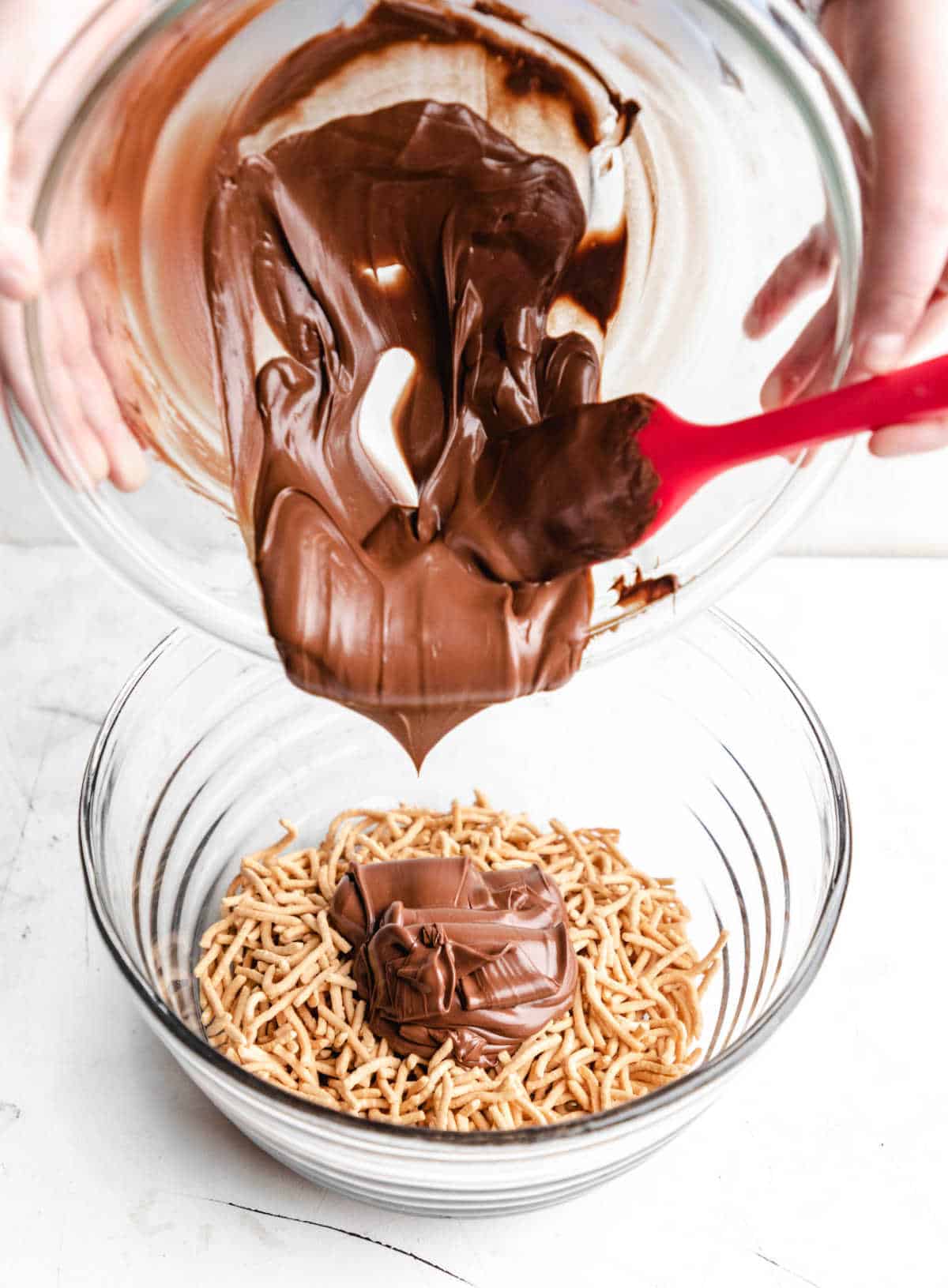 Melted chocolate mixture pouring onto chow mein noodles. 