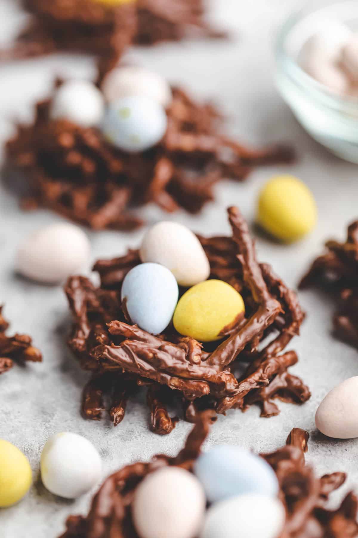 Bird's nest cookie next to a dish of candy eggs. 