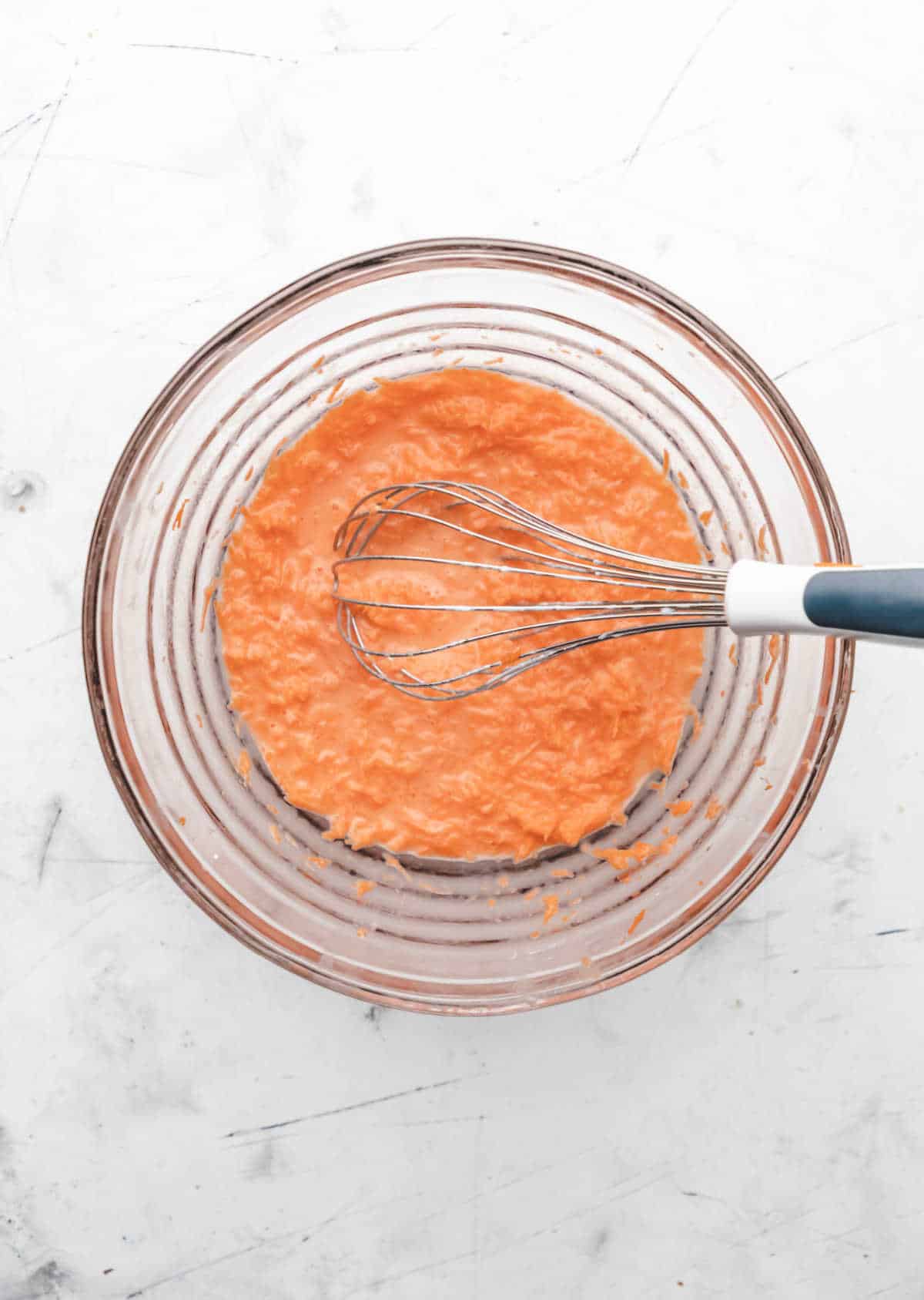 Shredded carrot whisked into wet ingredients in a glass mixing bowl. 