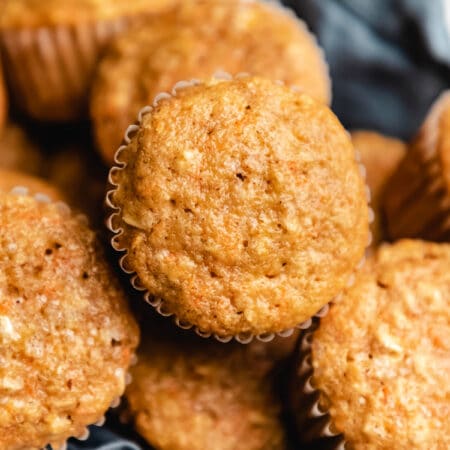 Cropped close up photo of several carrot oat muffins in a blue linen lined bread basket.