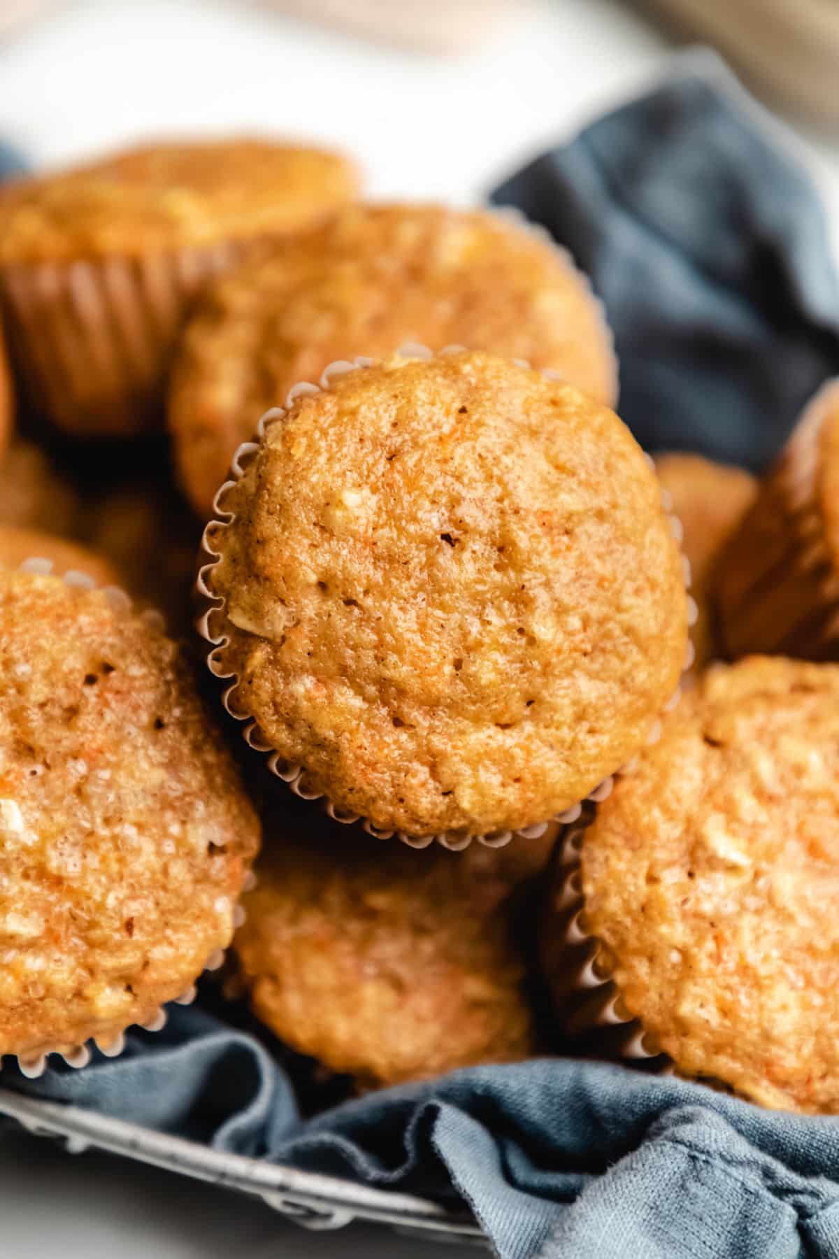 Cropped close up photo of several carrot oat muffins in a blue linen lined bread basket.