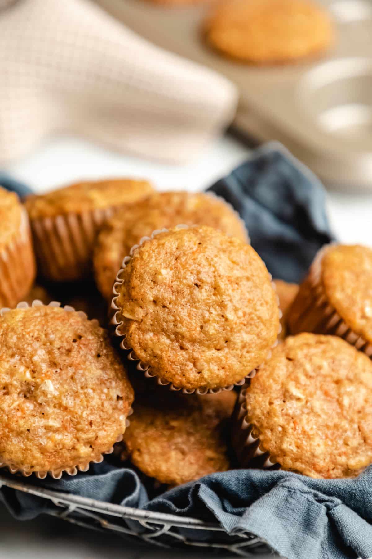 A bread basket lined with a blue linen napkin filled with carrot oat muffins.