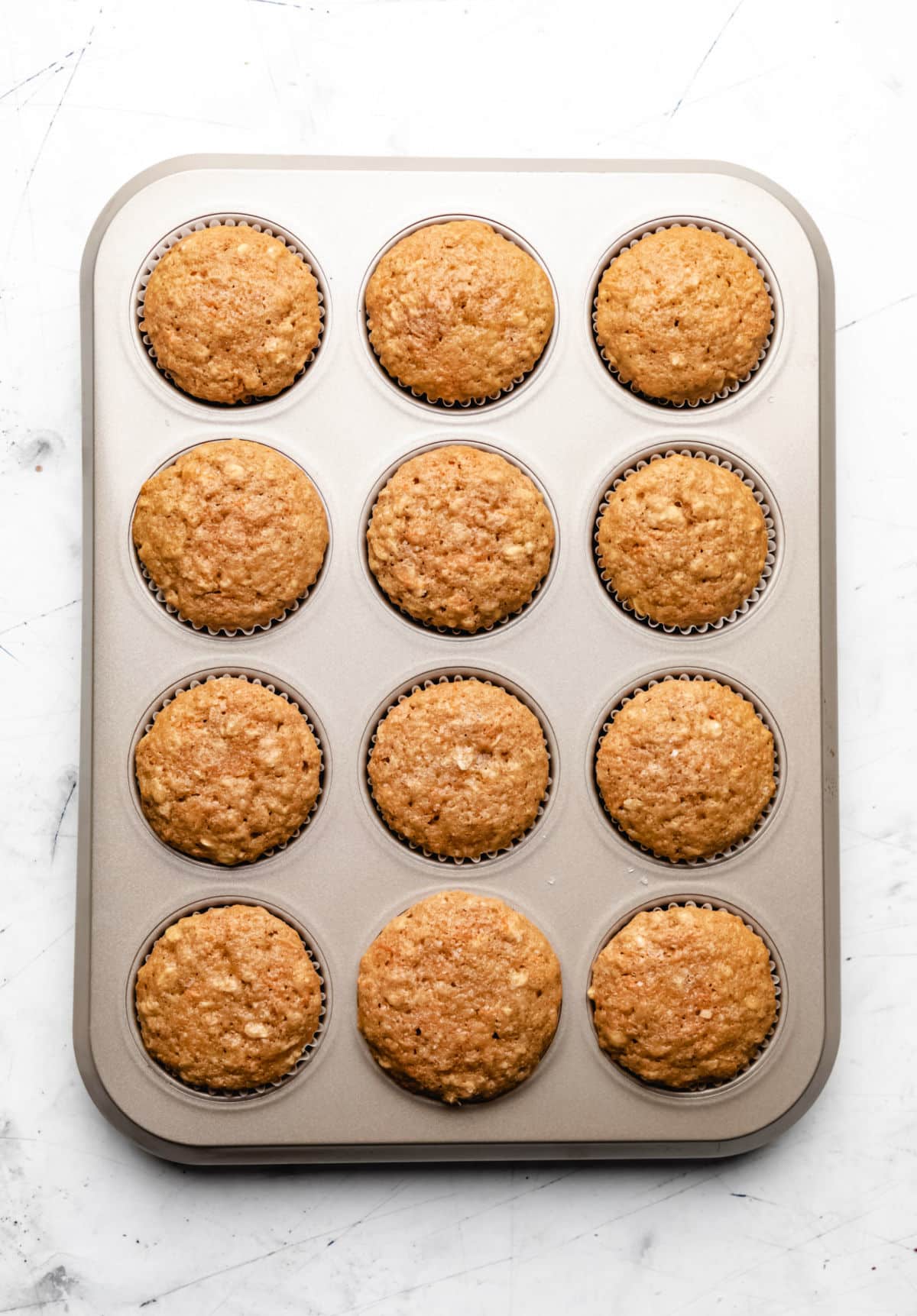 A dozen baked carrot oat muffins in a muffin tin. 