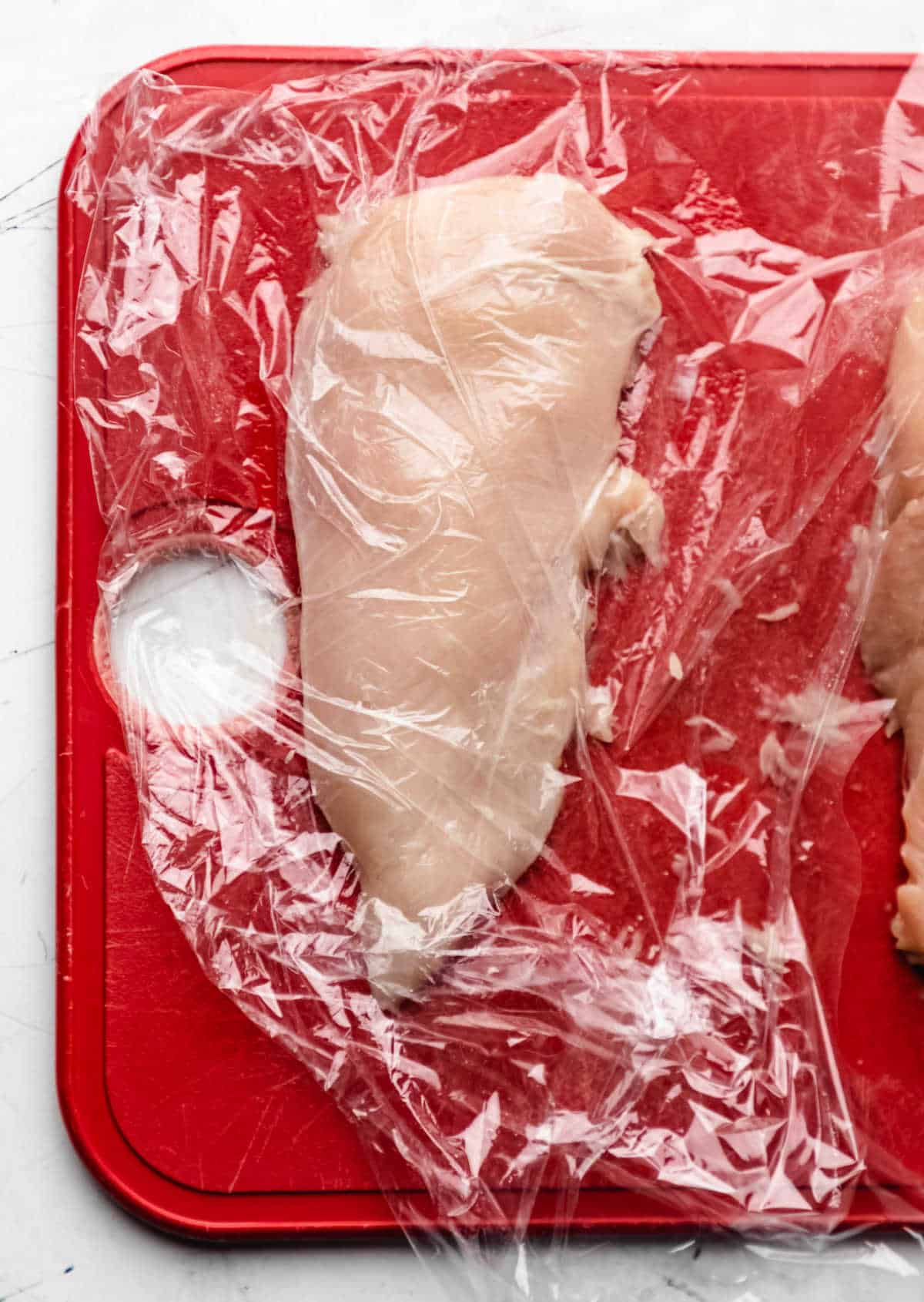 A chicken breast half under plastic wrap. 