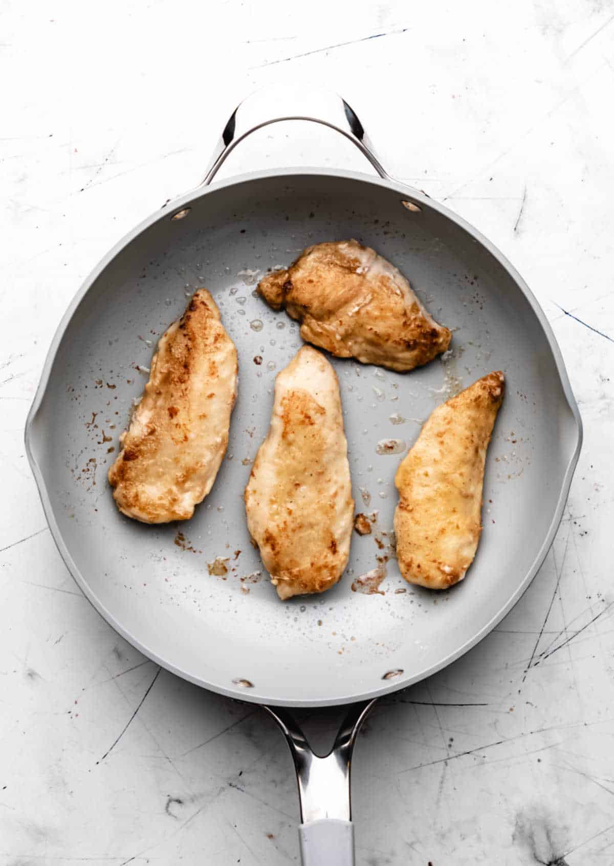 Four cooked chicken breast halves in a skillet. 