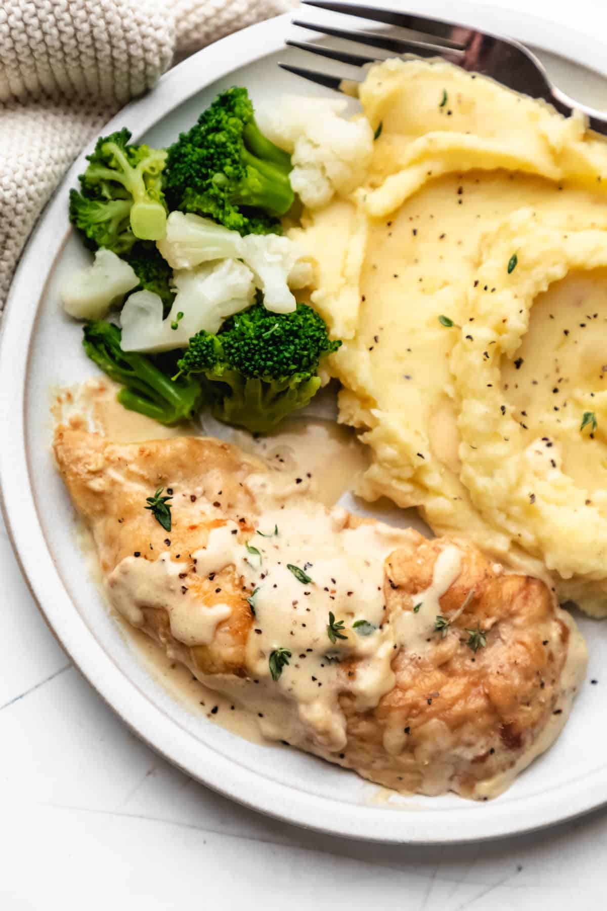Creamy mustard chicken on a plate next to steamed cauliflower and broccoli and mashed potatoes. 