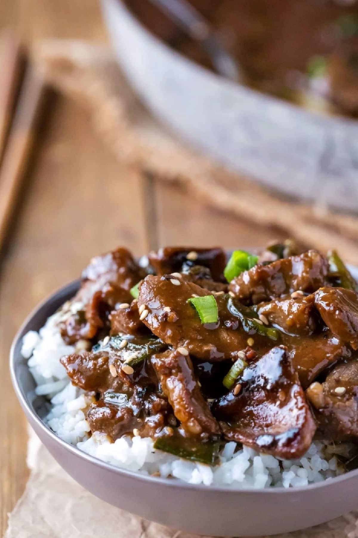 Mongolian beef over rice in a gray dish next to two wooden chopsticks. 