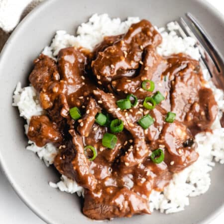 A gray dish of Mongolian beef topped with sliced green onions and toasted sesame seeds.