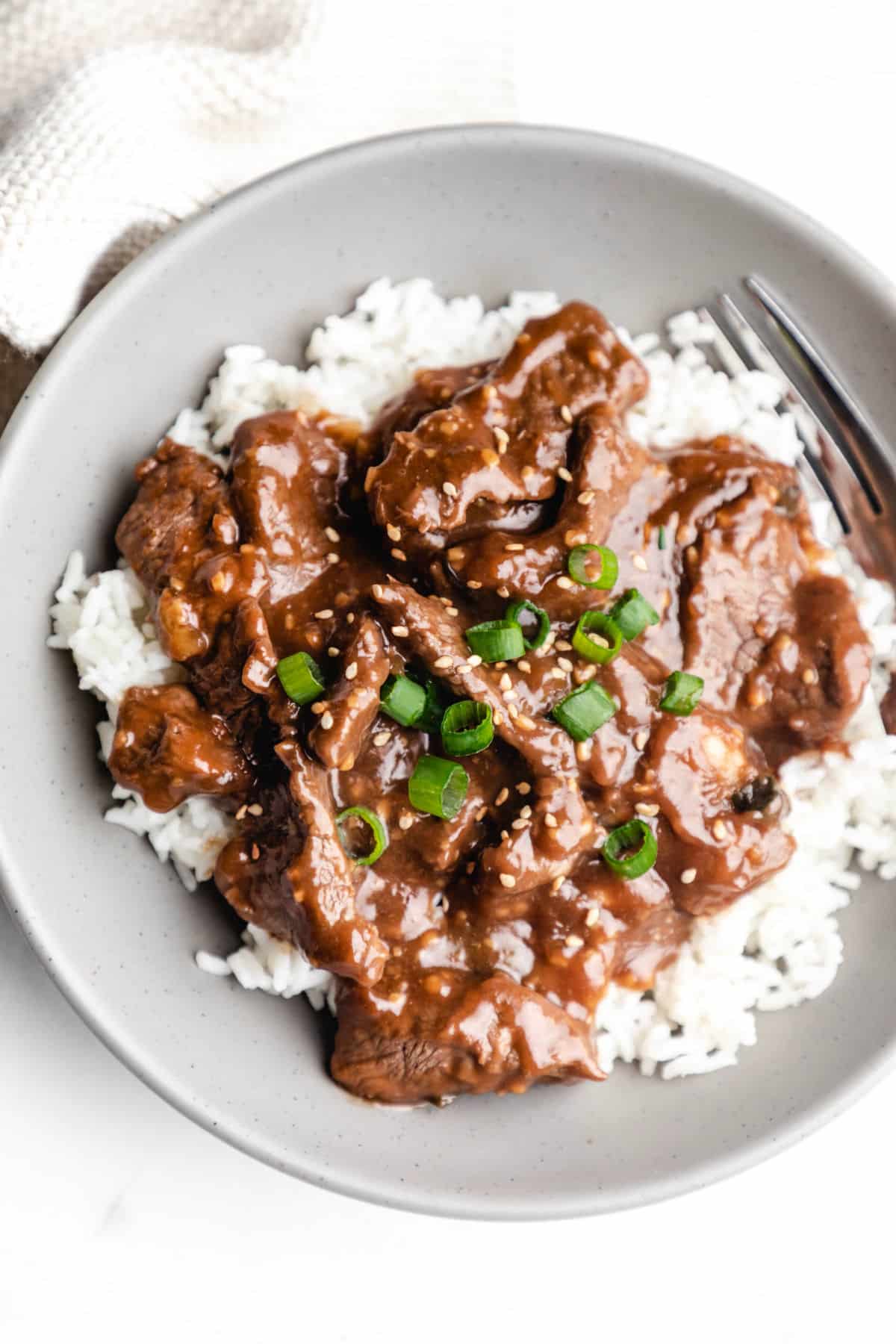 A gray dish of Mongolian beef topped with sliced green onions and toasted sesame seeds.