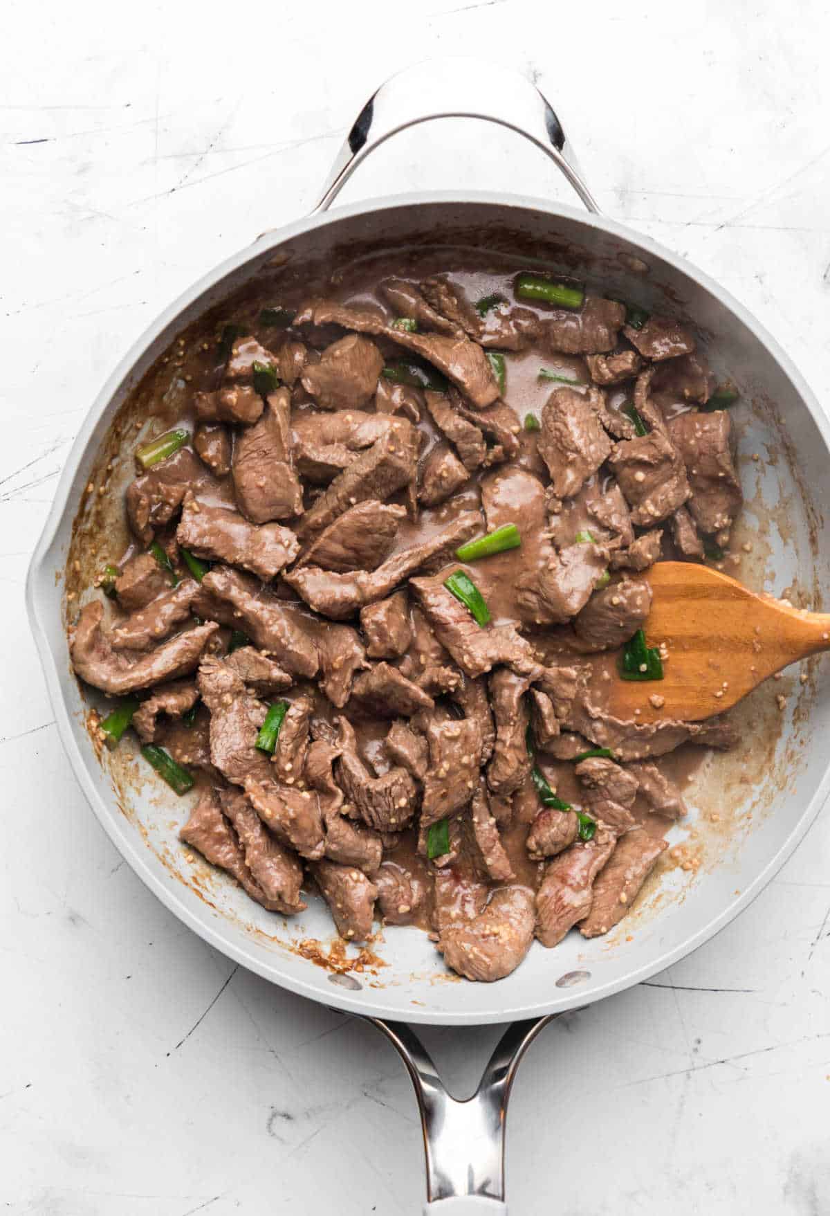 Green onions stirred into Mongolian beef in a large skillet.