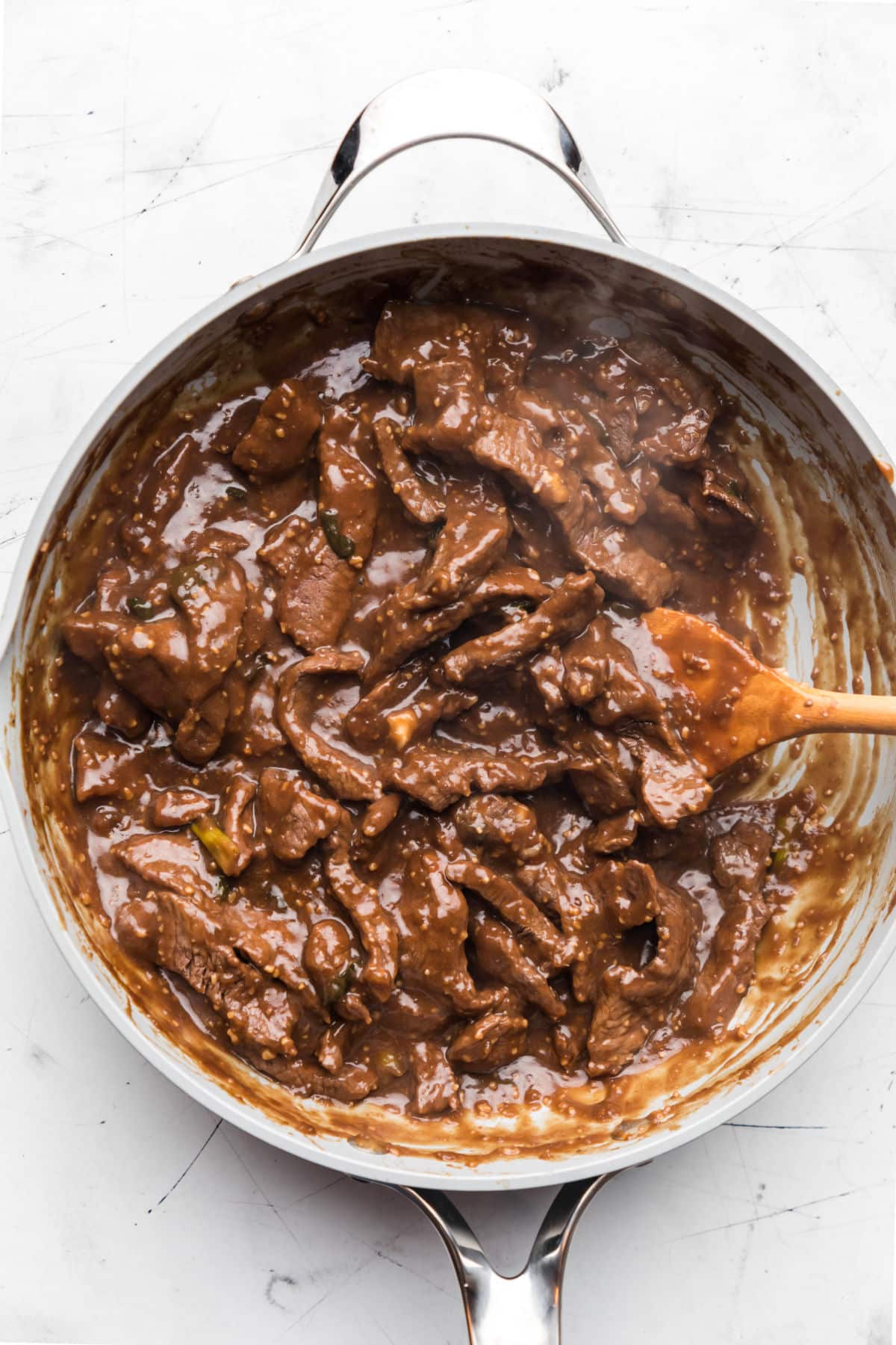 A wooden spoon stirring Mongolian beef in a large skillet. 