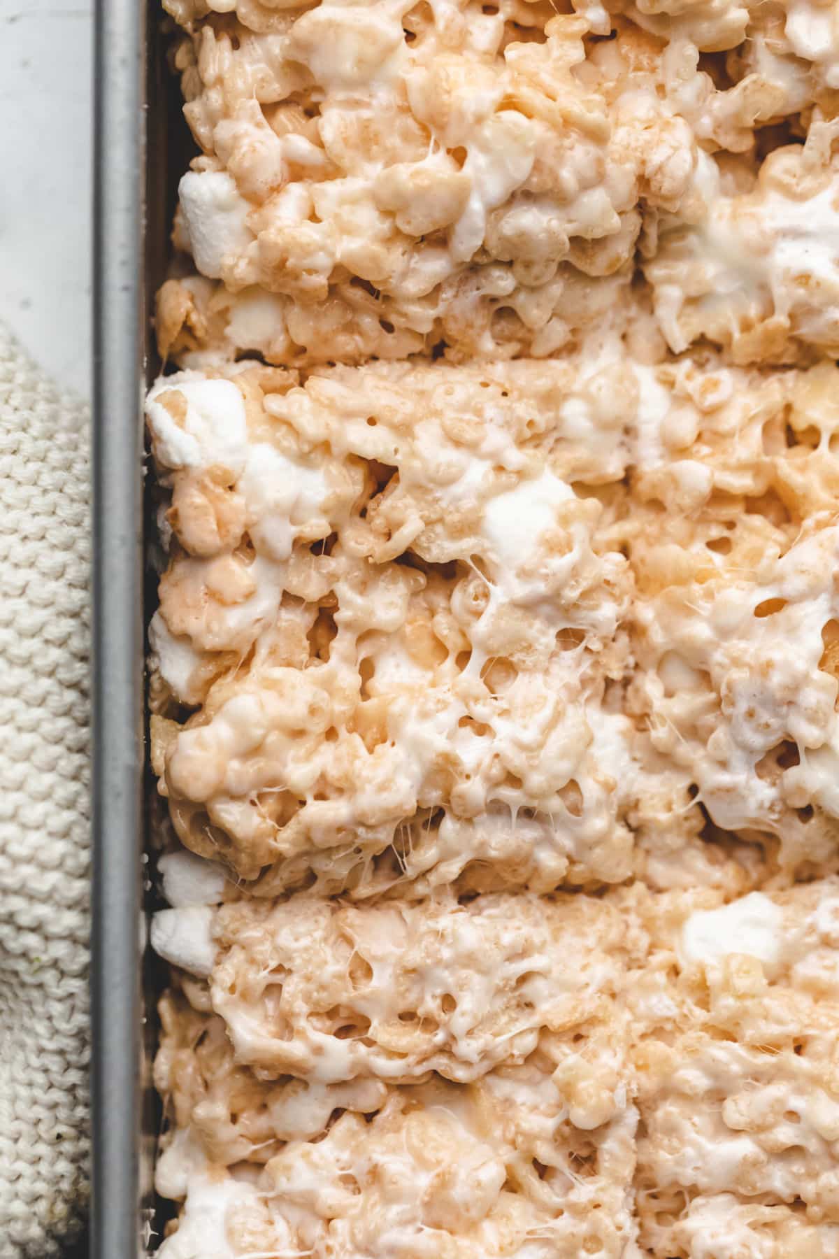 Close up photo of cut rice krispie treats in a silver baking pan. 