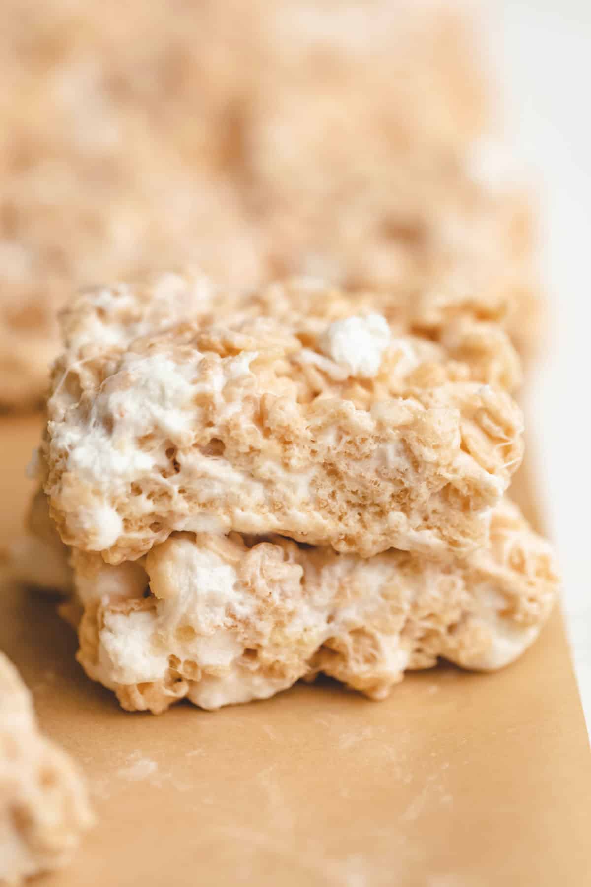 Two rice krispie treats on top of each other on a piece of brown parchment paper. 