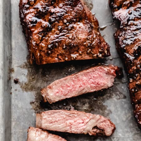 Three pieces of sliced steak next to the entire grilled steak.
