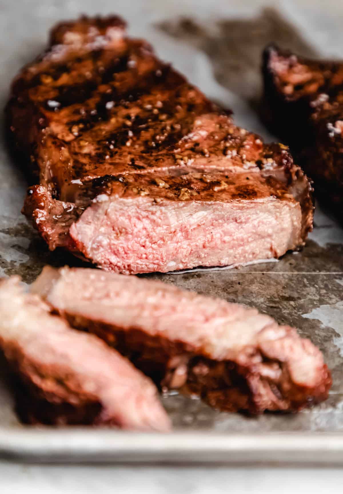 Steak with two pieces sliced off on a baking sheet. 