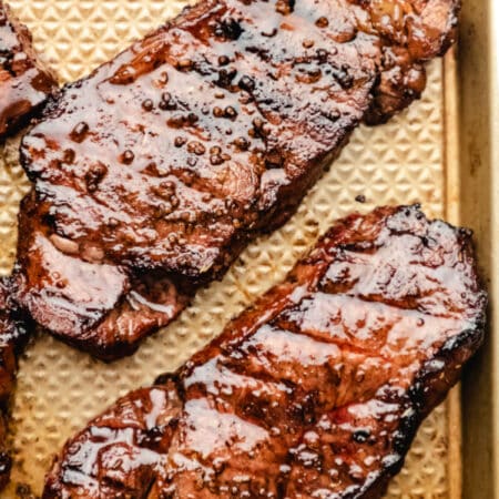 Grilled marinated steaks on a gold metal baking pan.