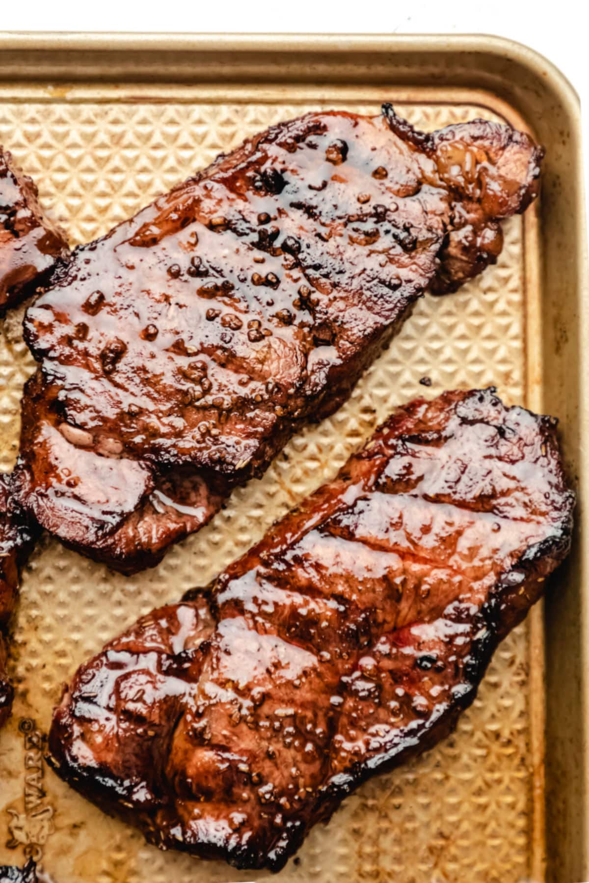 Grilled marinated steaks on a gold metal baking pan. 