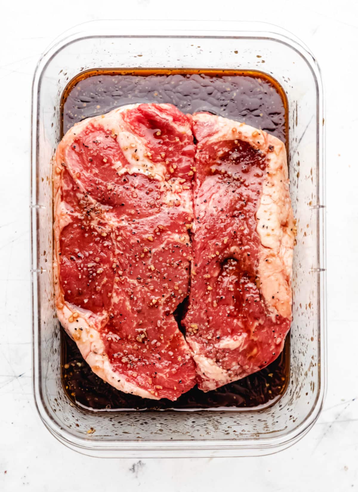 Two steaks in a container with marinade. 