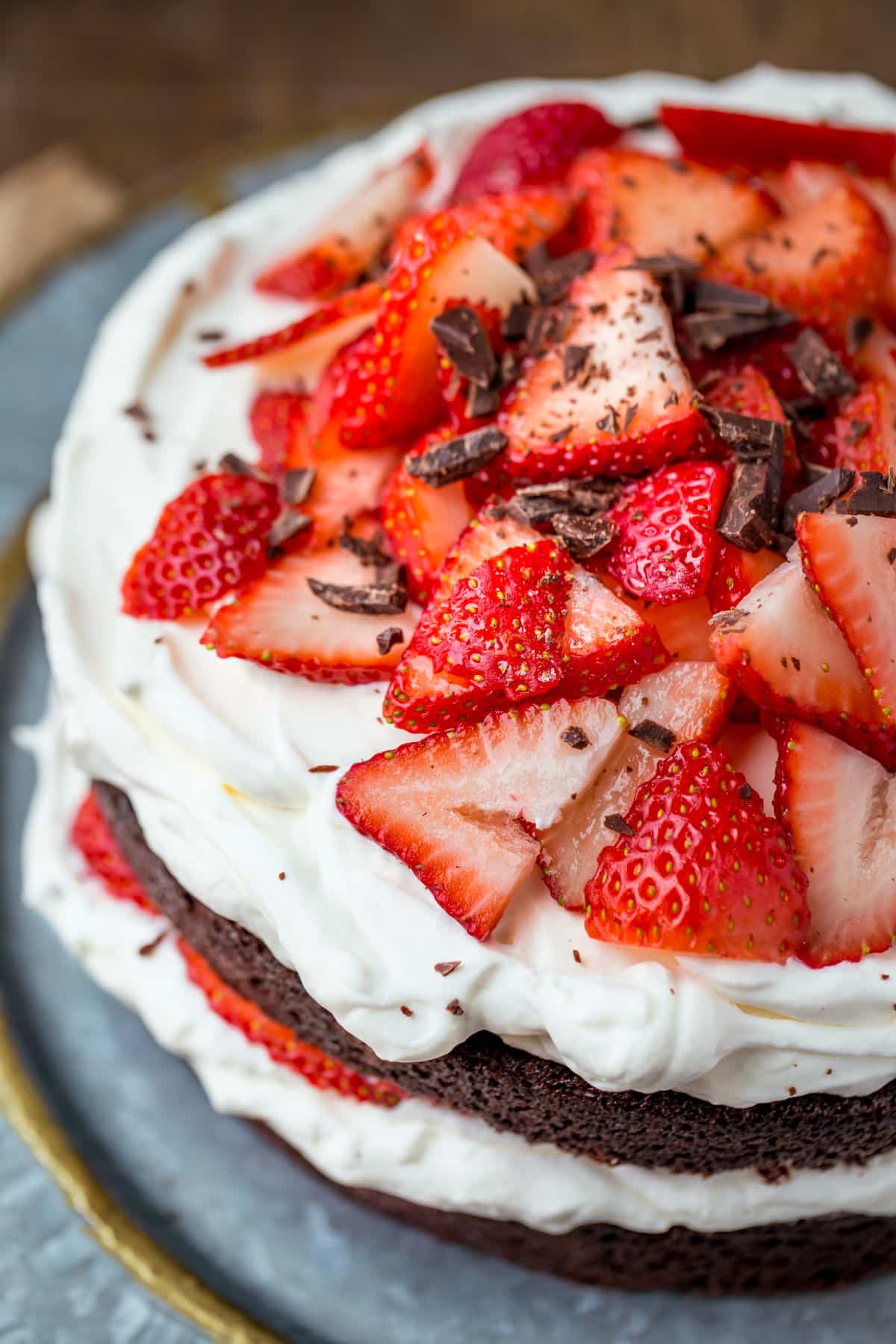 Strawberries and cream chocolate cake on a platter with plates and silverware in the background.