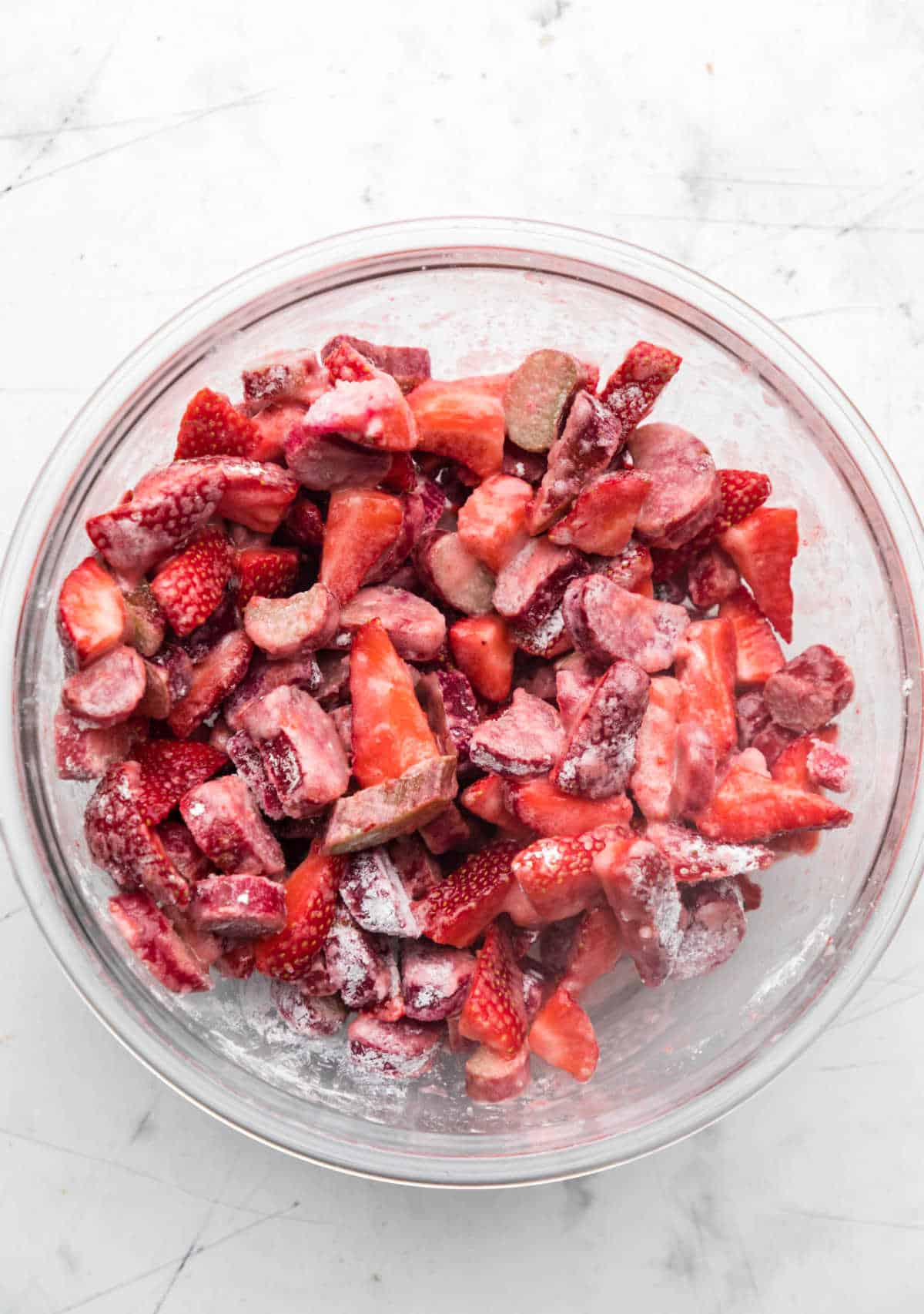 Sliced strawberries rhubarb and cornstarch in a glass mixing bowl. 