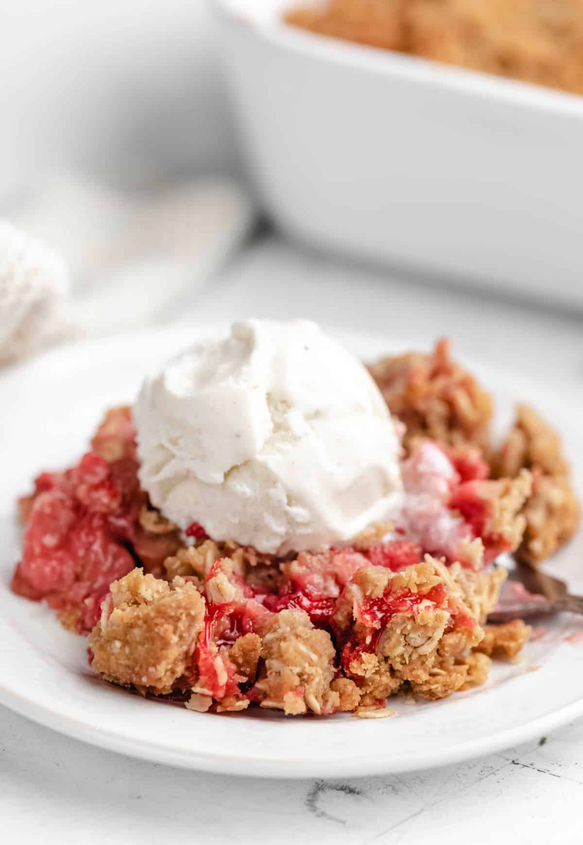 A dish of strawberry rhubarb crisp topped with a scoop of vanilla ice cream.