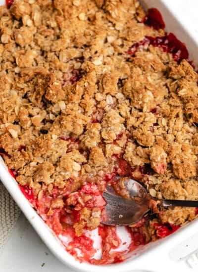 A silver spoon scooping out strawberry rhubarb crisp.