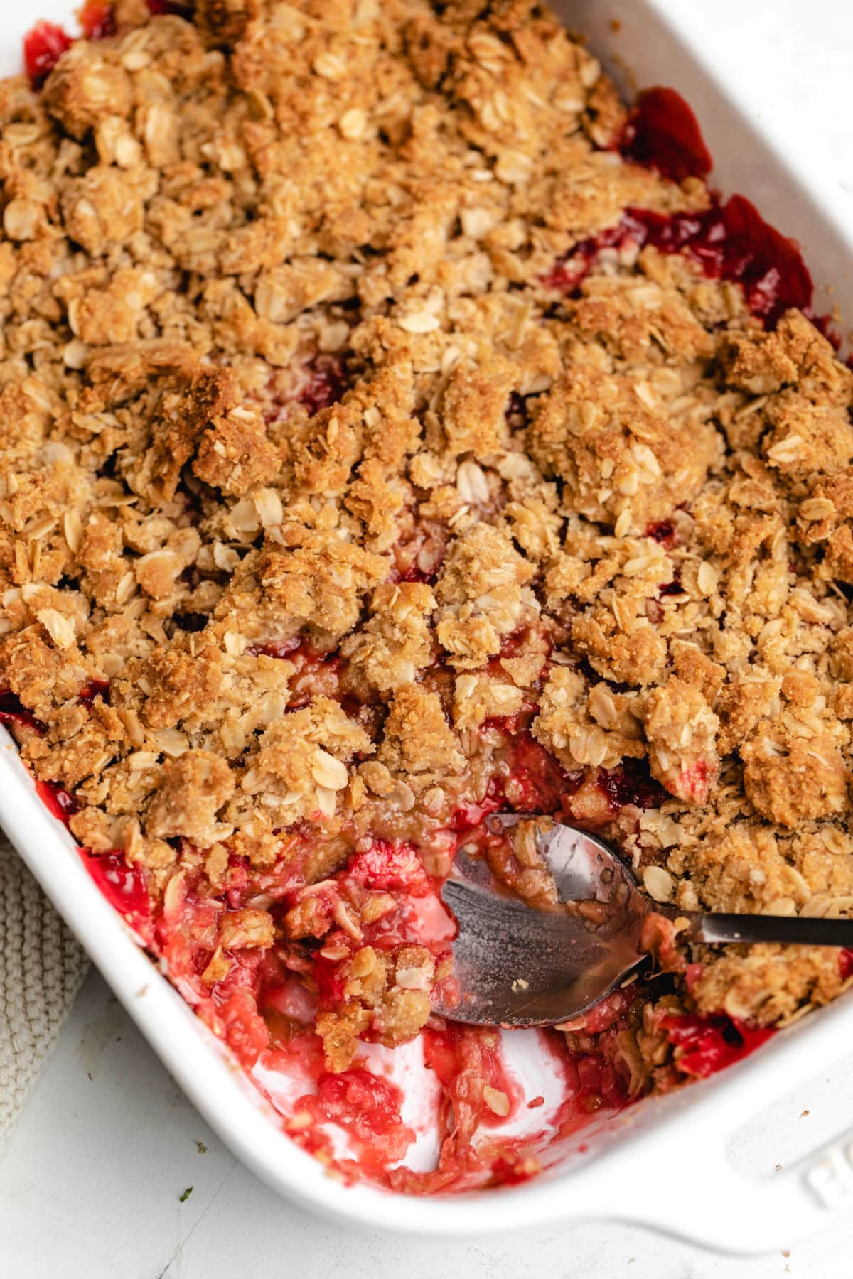 A silver spoon scooping out strawberry rhubarb crisp. 