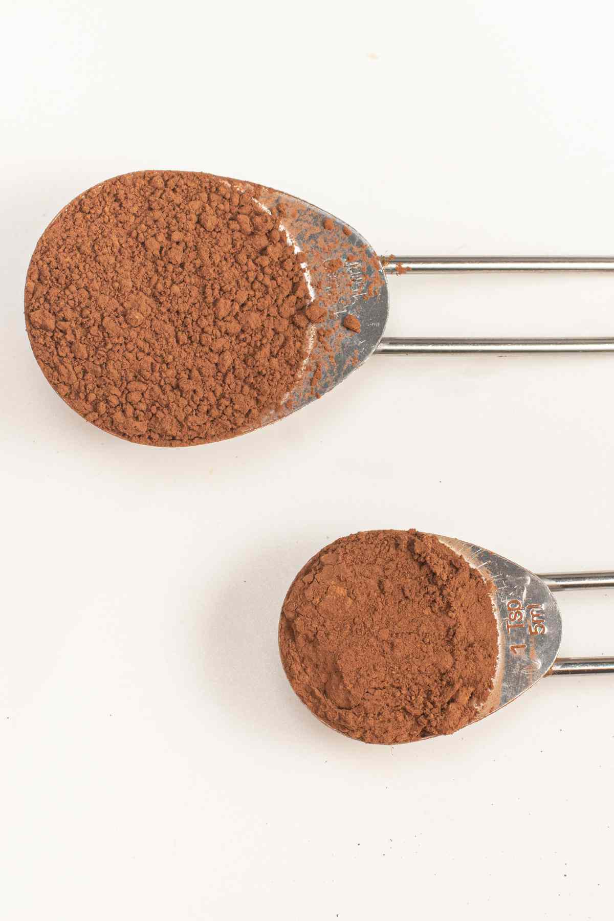 A teaspoon and a tablespoon with cocoa powder in them.