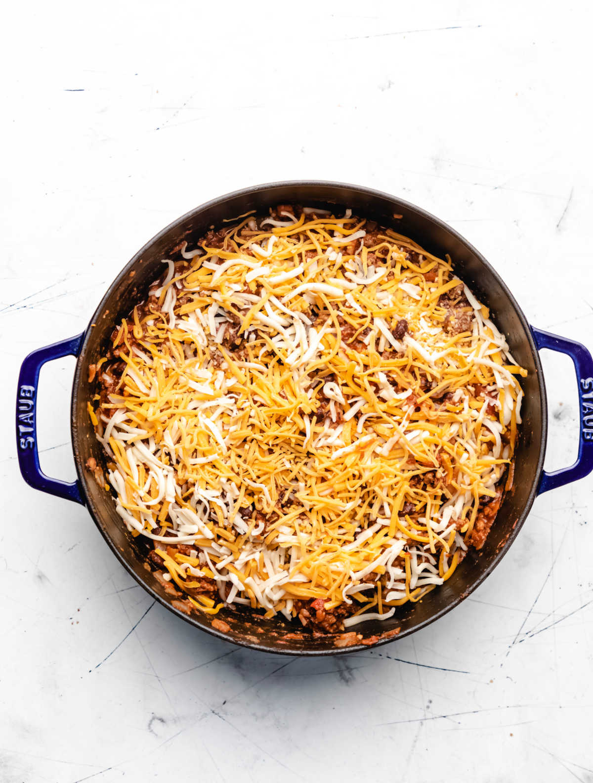 Shredded cheese on top of taco casserole in a skillet. 