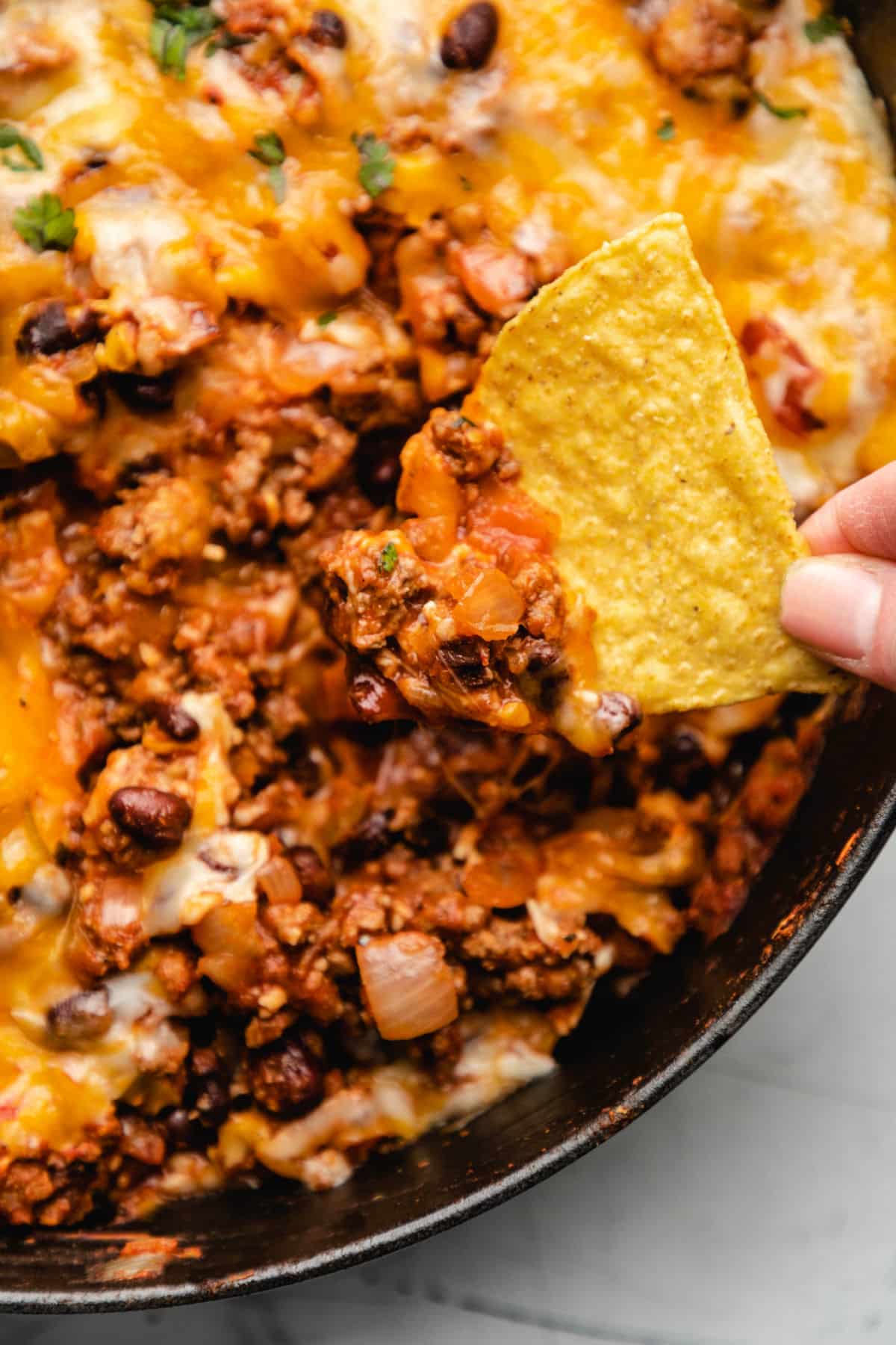 A hand holding a tortilla chip in taco casserole. 