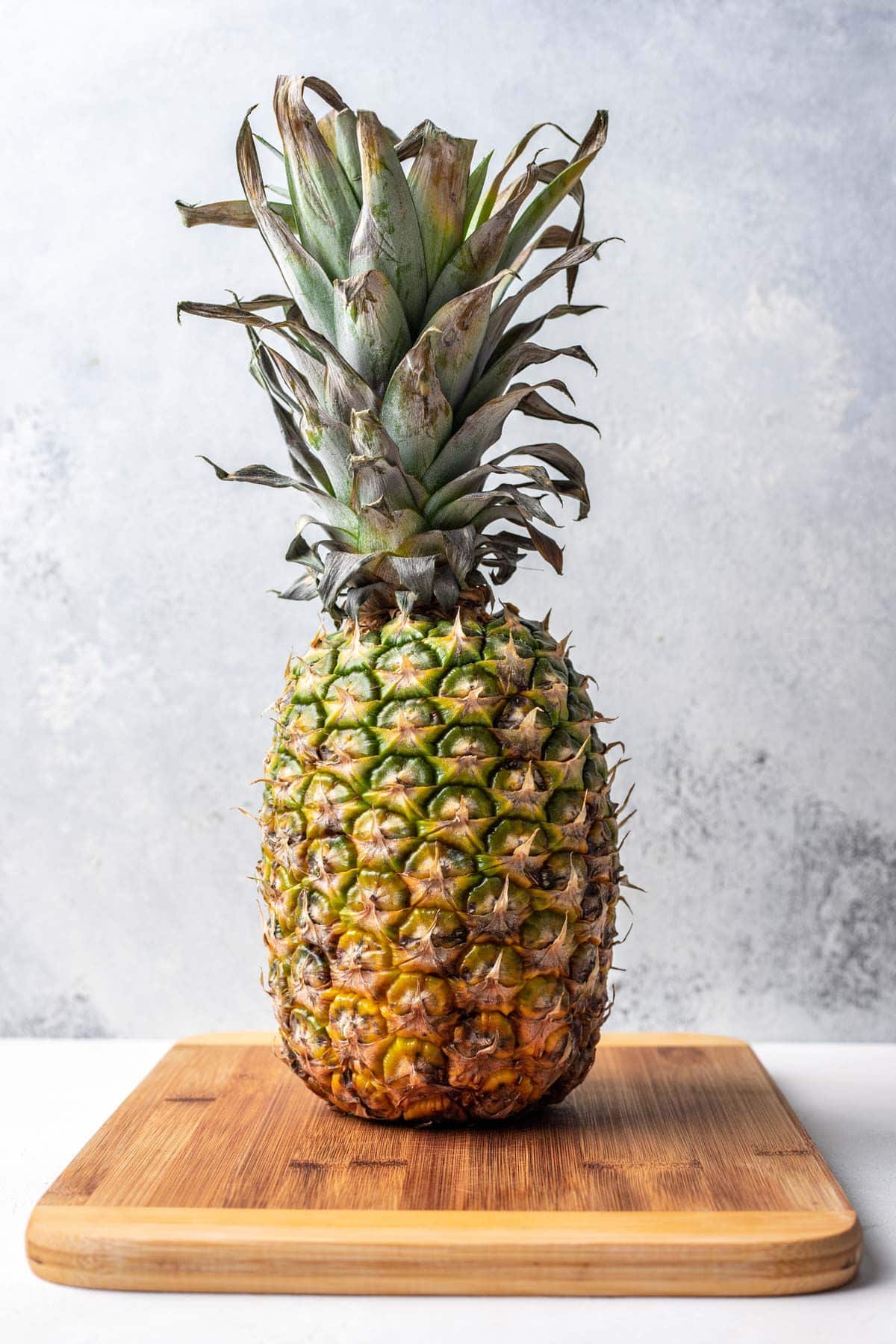 A whole fresh pineapple sitting on a wooden cutting board. 
