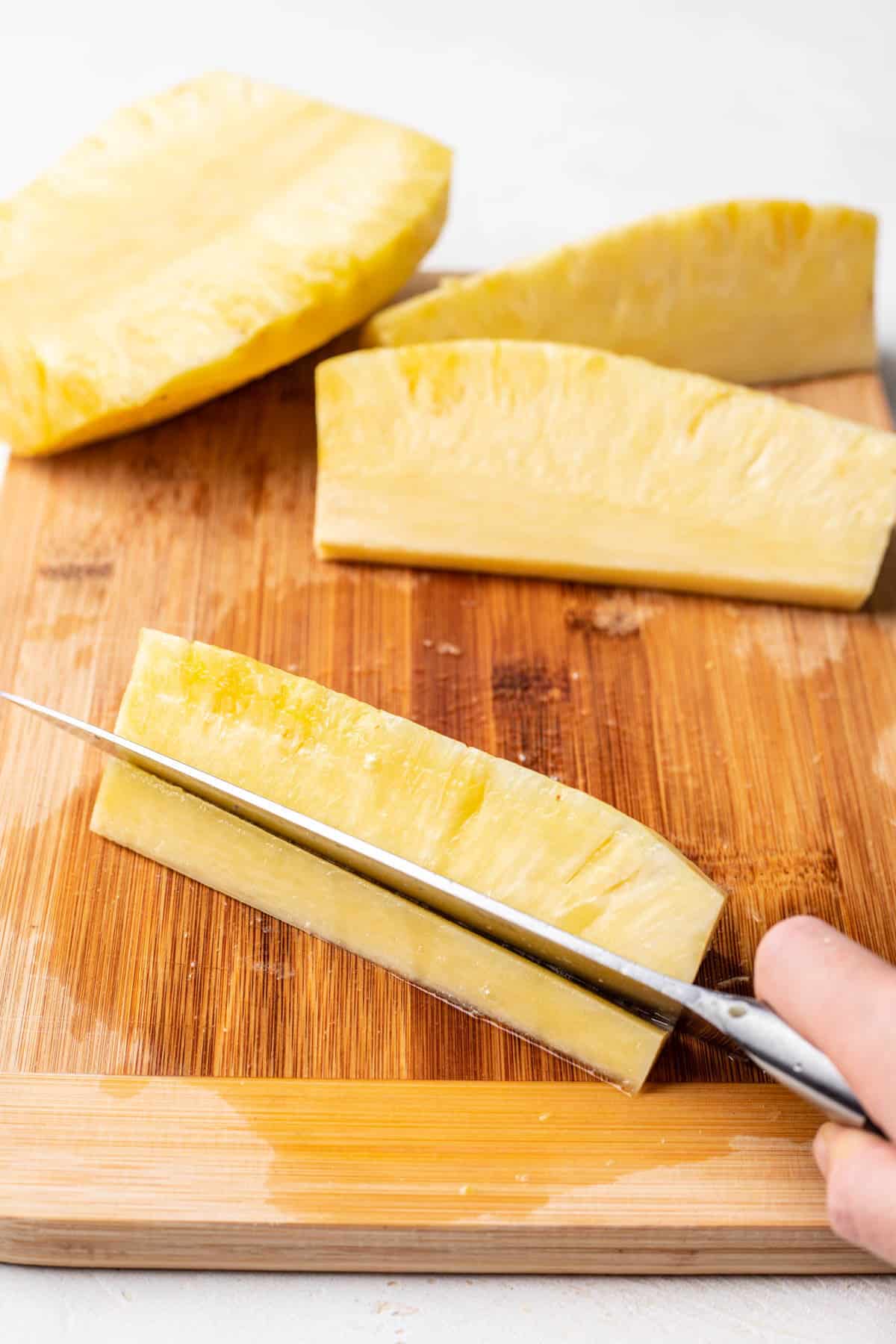 A knife cutting the core off of the pineapple spear. 