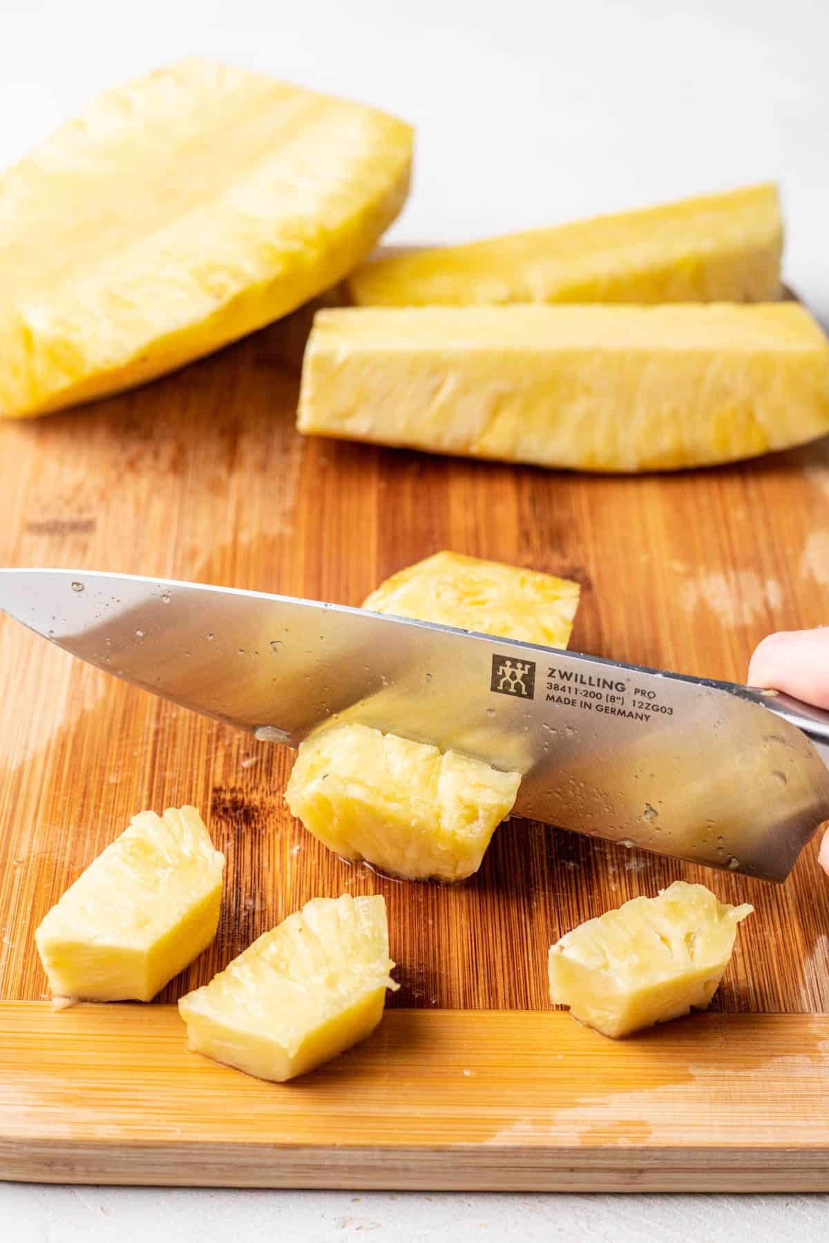 A knife cutting chunks of pineapple from a pineapple spear. 